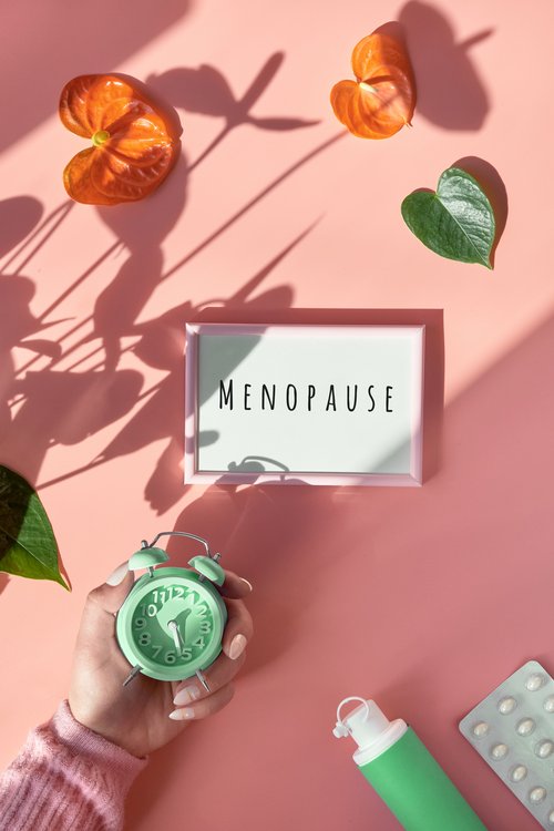 ext Menopause on light box in hand. HRT Replacement hormone therapy, HRT concept. Pink background with exotic leaves, flowers, pills, estrogene gel